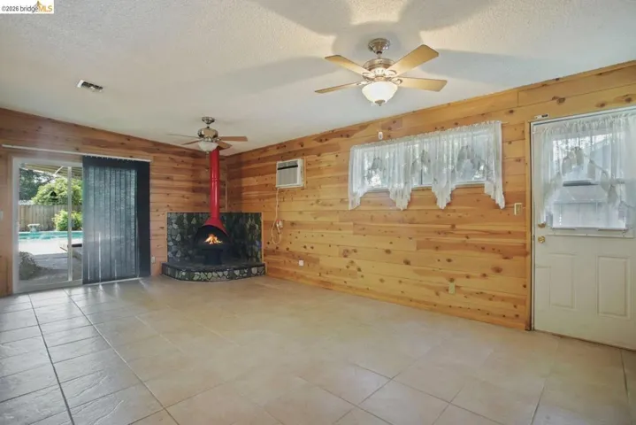 Unfurnished living room featuring wood walls, ceiling fan, and a textured ceiling