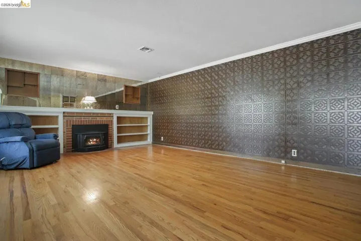 Unfurnished living room featuring ornamental molding, light wood finished floors, and a brick fireplace