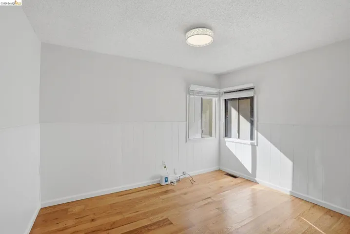 Unfurnished room with a textured ceiling, a wainscoted wall, and light wood-style flooring
