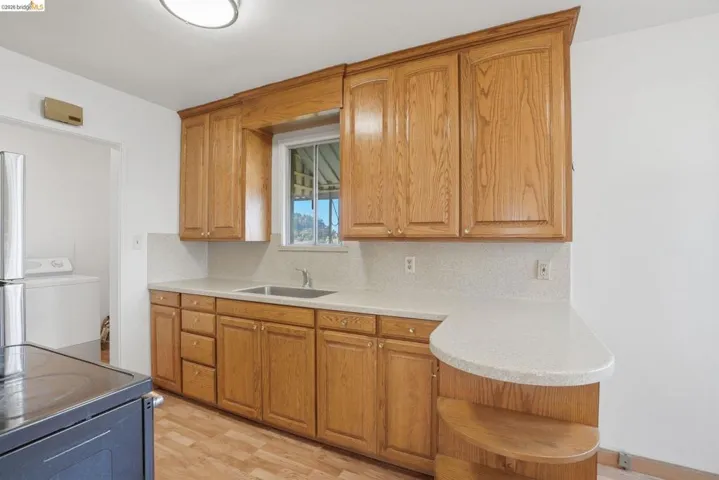 Kitchen with decorative backsplash, light wood-style flooring, washer / clothes dryer, electric range oven, and open shelves