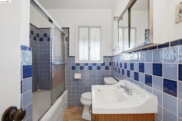 Bathroom with vanity, enclosed tub / shower combo, tile walls, and a wainscoted wall