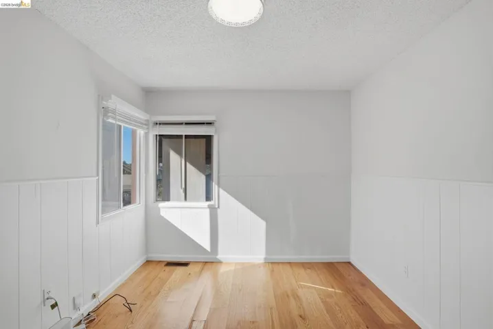Unfurnished room featuring light wood-style floors, wainscoting, and a textured ceiling