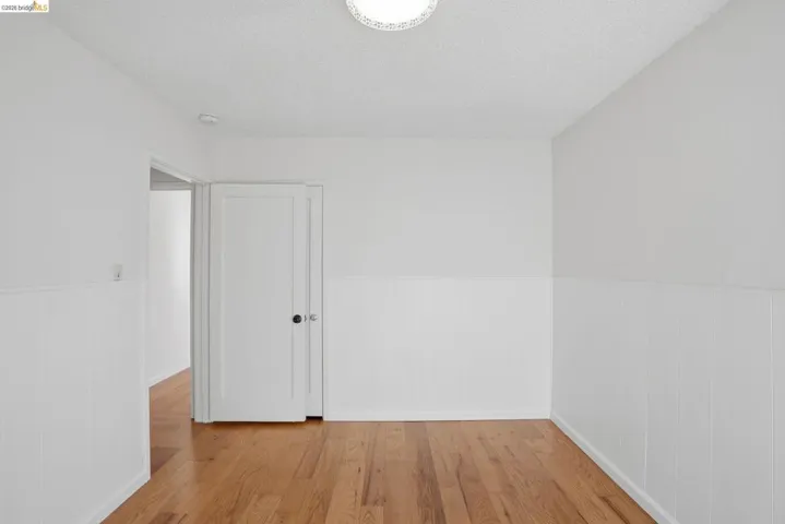 Empty room featuring wainscoting, light wood-type flooring, and a textured ceiling