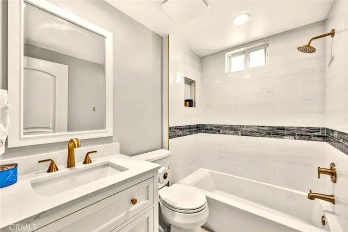 Remodeled bathroom featuring quartz countertop vanity, designer fixtures, and tiled shower/tub combination.