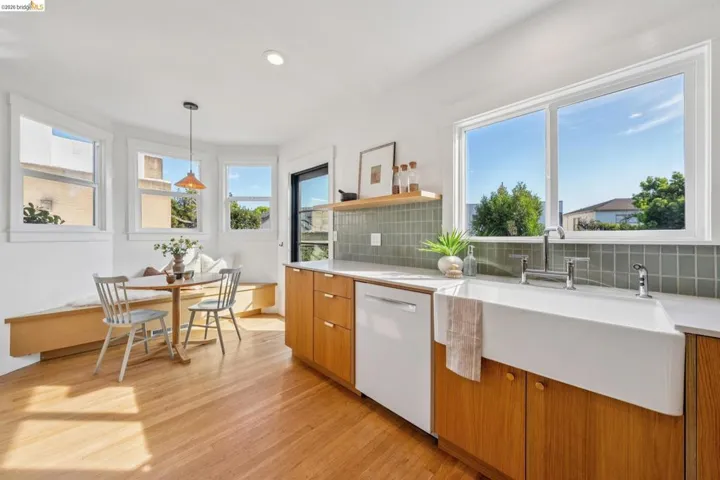 Kitchen featuring breakfast area, decorative backsplash, dishwasher, open shelves, and light wood-style flooring