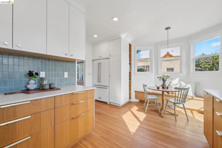 Dual tone kitchen featuring high end white fridge, decorative light fixtures, light wood finished floors, two tone color scheme, and decorative backsplash