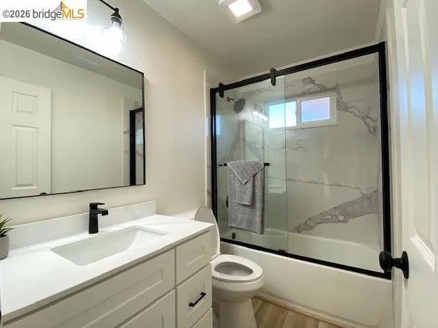 Full bath featuring vanity, shower / bath combination with glass door, and light wood-style floors