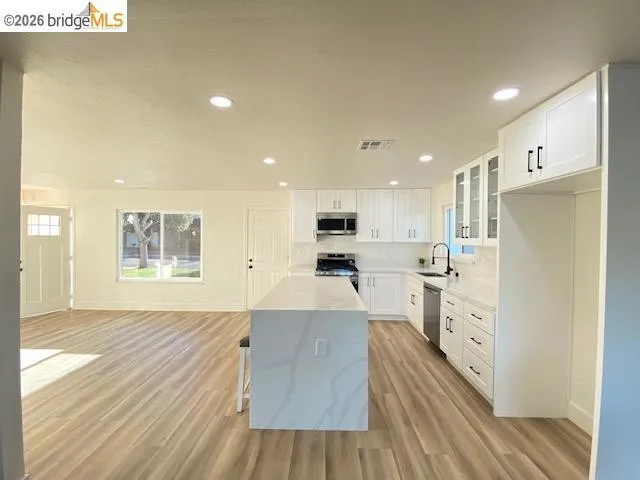 Kitchen with glass fronted cabinets, white cabinetry, stainless steel appliances, light wood-style floors, and recessed lighting