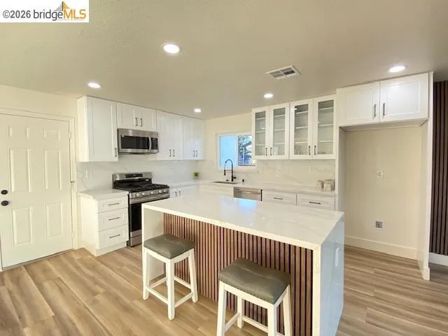 Kitchen featuring glass insert cabinets, stainless steel appliances, white cabinetry, light wood-style floors, and a kitchen island