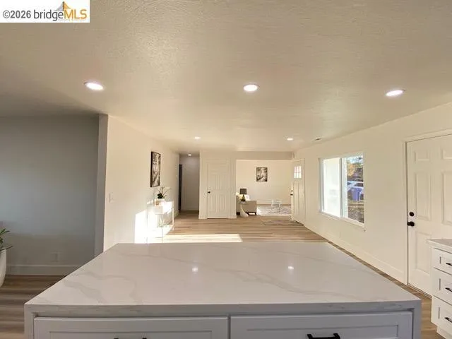 Kitchen with light wood finished floors, white cabinetry, a center island, light stone countertops, and recessed lighting