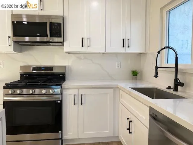Kitchen featuring stainless steel appliances, white cabinetry, and light stone countertops