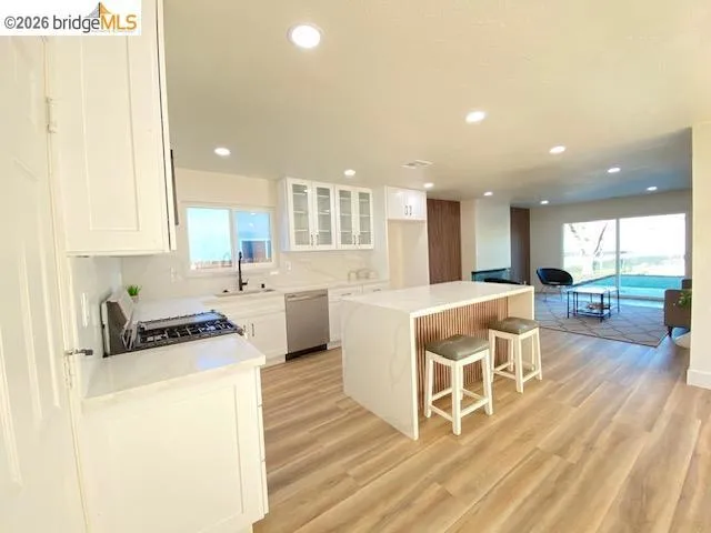 Kitchen with glass fronted cabinets, a kitchen island, a breakfast bar area, white cabinetry, and light wood-type flooring