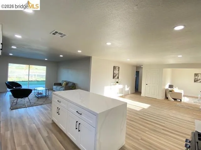 Kitchen with open floor plan, a kitchen island, white cabinetry, light wood-style floors, and recessed lighting
