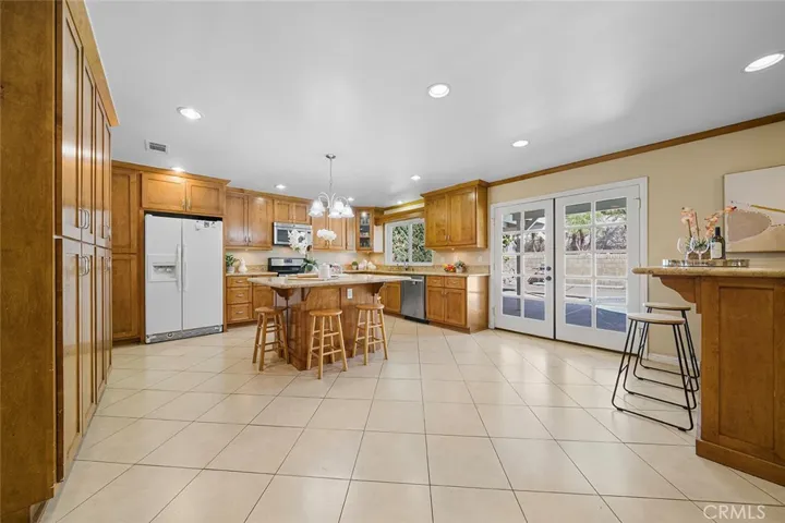 Straight from the entry leads to an inviting updated kitchen, at one time, reimagined with extra cabinets for pantry needs and room to enjoy as extra living room. Island in the middle is a great gathering hub with granite counters. Wet bar to the right of the image makes it perfect for entertaining. French doors leads to the covered patio and poo.
