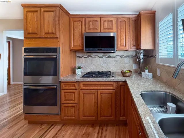 Kitchen featuring stainless steel appliances, wood finish cabinets, and light stone countertops