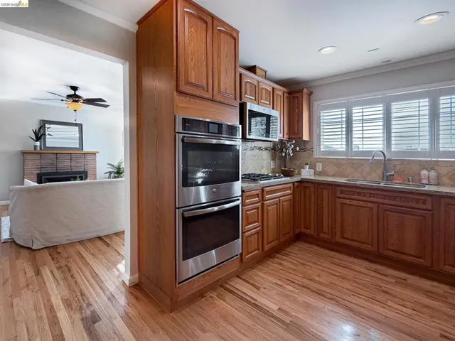 Kitchen featuring crown molding, stainless steel appliances, wood finish cabinetry, decorative backsplash, and light wood-type flooring