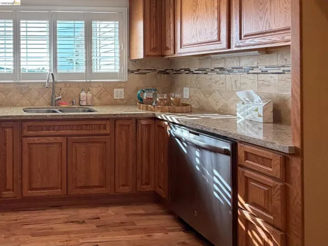 Kitchen with stainless steel dishwasher, wood finish cabinets, light wood finished floors, and light stone countertops