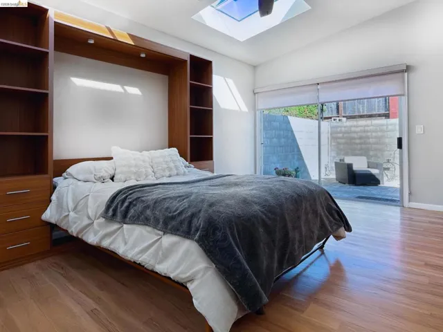 Bedroom featuring vaulted ceiling, a skylight, light wood-type flooring, and access to exterior