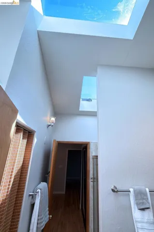 Bathroom with a skylight, a textured wall, wood finished floors, and a shower with shower door