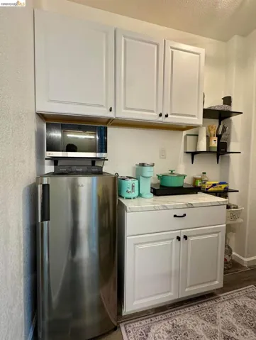 Bar featuring white cabinets, stainless steel fridge, light countertops, a textured wall, and a textured ceiling