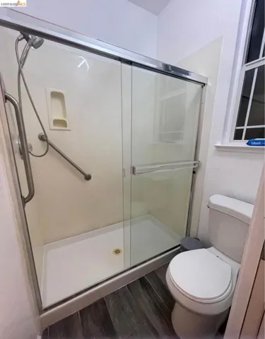 Bathroom featuring a stall shower, dark wood finished floors, and a textured wall