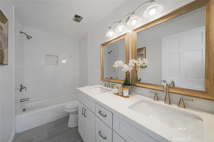Reimagined primary bathroom newly updated that now has double sinks along with new cabinet, fixtures, mirror, counter, cast iron tub, tile.