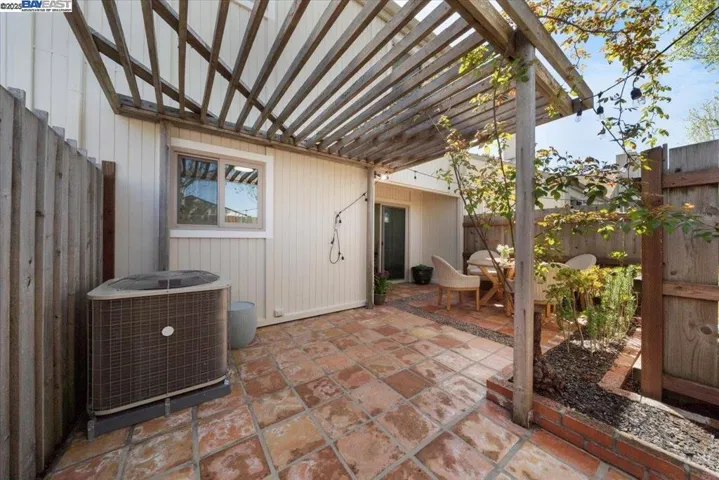 An inviting stone patio with a romantic trellis, draped in seasonal roses and glowing string lights.