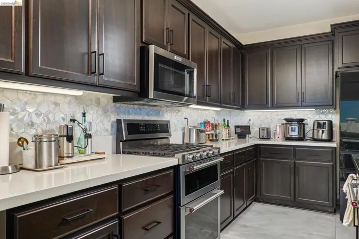 Kitchen featuring dark wood finish cabinetry, stainless steel appliances, decorative backsplash, and light stone counters