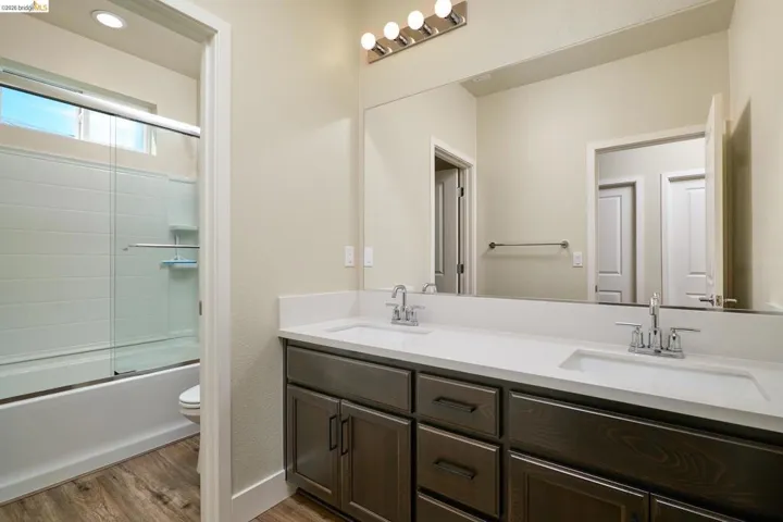 Full bath featuring double vanity, light wood-style floors, and combined bath / shower with glass door
