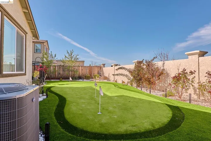 Fenced backyard featuring a putting green and a patio