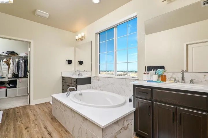 Full bath with a garden tub, a walk in closet, two vanities, and light wood-style floors