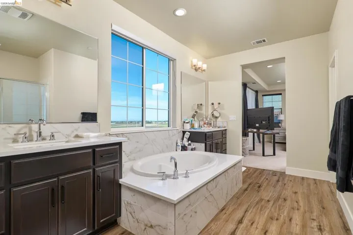 Bathroom with a bath, light wood finished floors, two vanities, a shower stall, and recessed lighting
