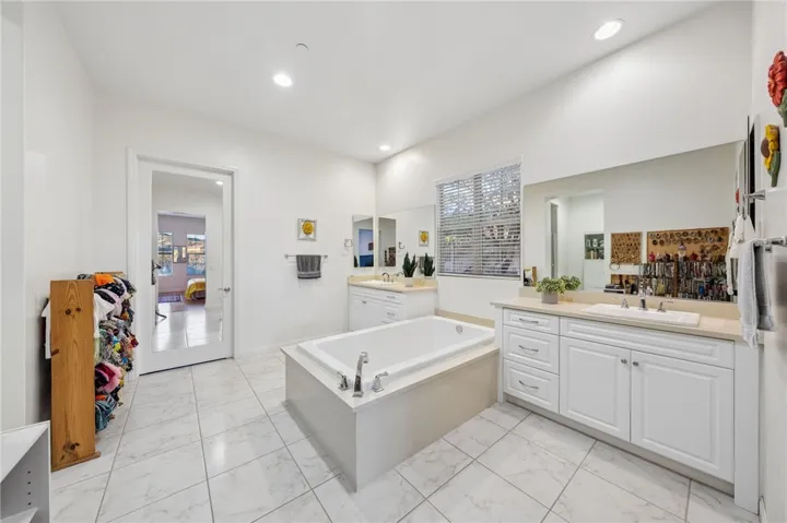 Spacious primary bath features dual vanities, oversized tile flooring, and a soaking tub set in a bright, open layout.