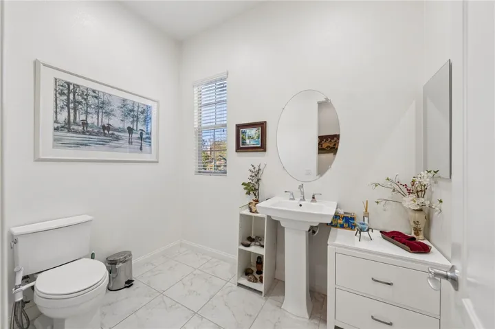 Bright guest bath features a pedestal sink, oversized tile flooring, and a clean, airy design.