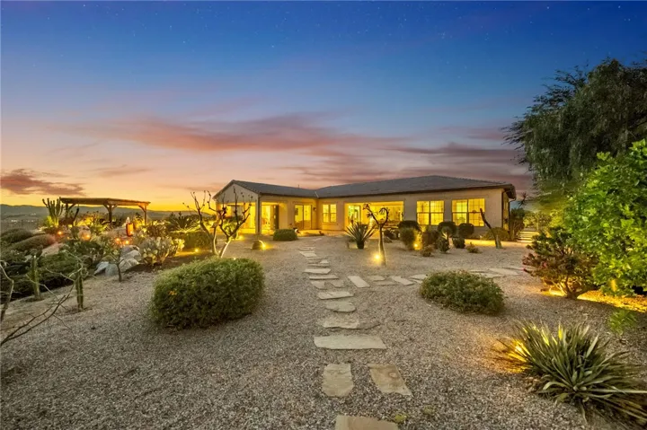 Resort-style backyard with illuminated landscape lighting, gravel hardscape, and a spacious patio area designed for relaxing evenings outdoors.