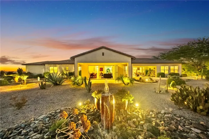 Covered rear patio opens to a beautifully lit backyard with decorative water feature and expansive outdoor living space.