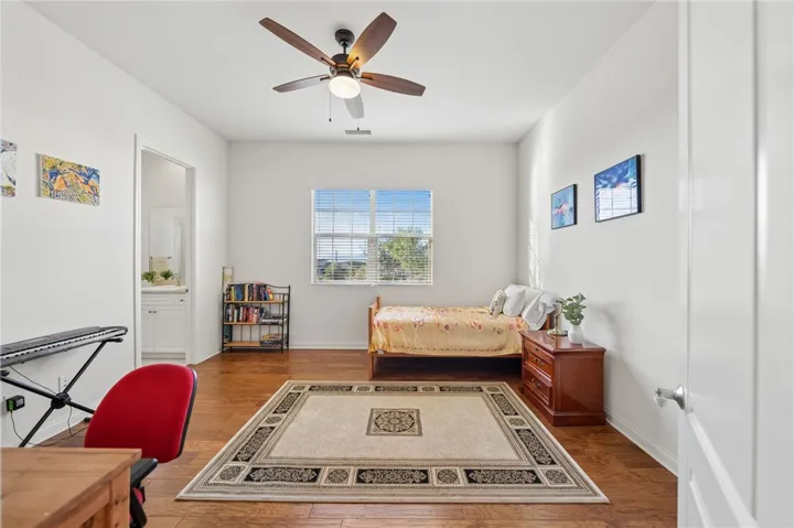 Spacious bedroom includes warm wood flooring, abundant natural light, and convenient access to a private vanity area.