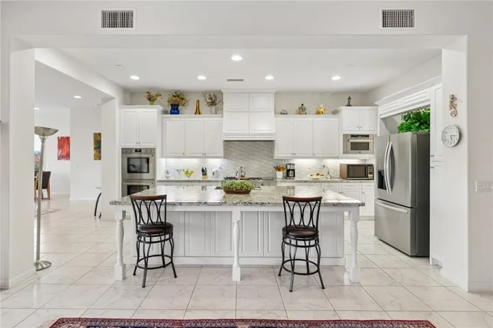 Bright kitchen showcases an oversized island, granite countertops, extensive white cabinetry, and stainless steel appliances.