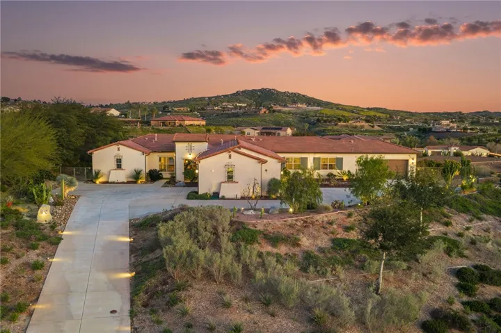 Twilight front elevation showcases the home’s impressive footprint, long driveway, and softly lit desert landscaping.