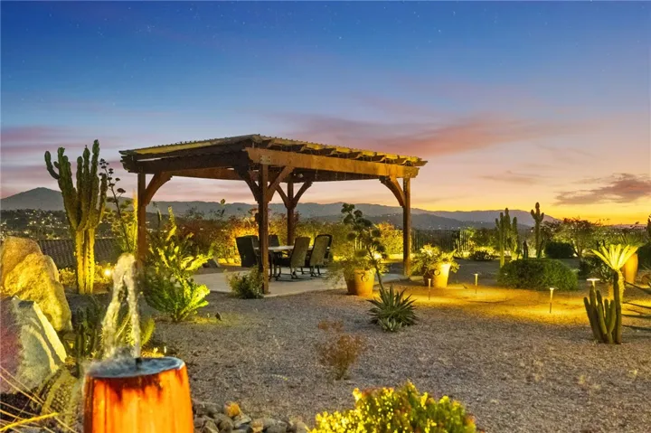 Freestanding pergola creates a comfortable outdoor dining area surrounded by mature desert landscaping and scenic sunset views.