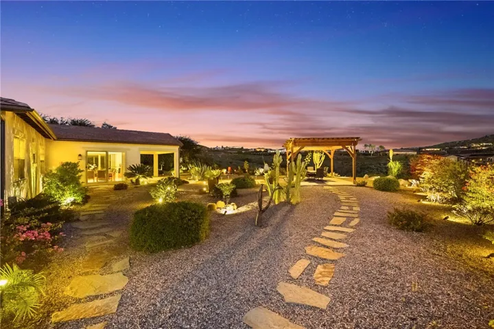 Meandering stone paths, accent lighting, and drought-conscious landscaping create a warm and welcoming outdoor setting.