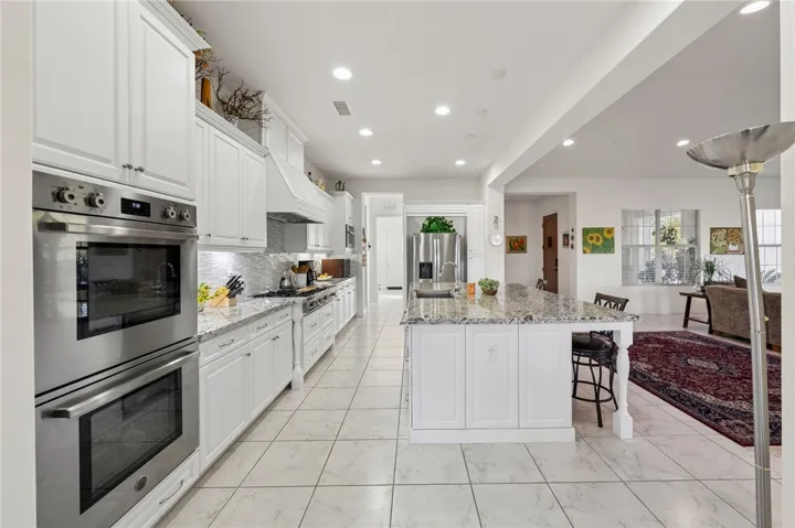 Generous center island with bar seating anchors the kitchen, complemented by double wall ovens, a gas cooktop, and stylish tile backsplash.