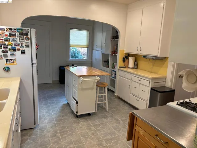 Kitchen with arched walkways, freestanding refrigerator, a kitchen breakfast bar, white cabinets, and wood counters