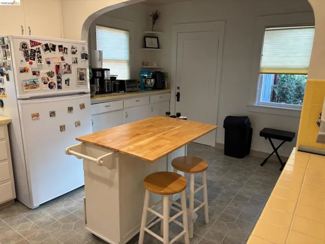 Kitchen featuring freestanding refrigerator, arched walkways, white cabinets, a kitchen breakfast bar, and wooden counters