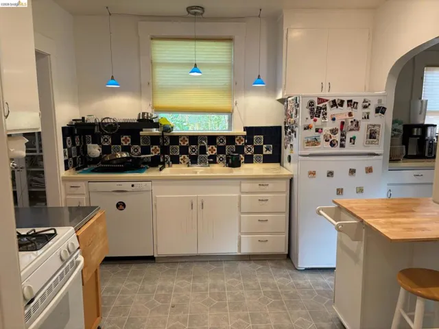 Kitchen with white appliances, butcher block countertops, white cabinetry, and hanging light fixtures