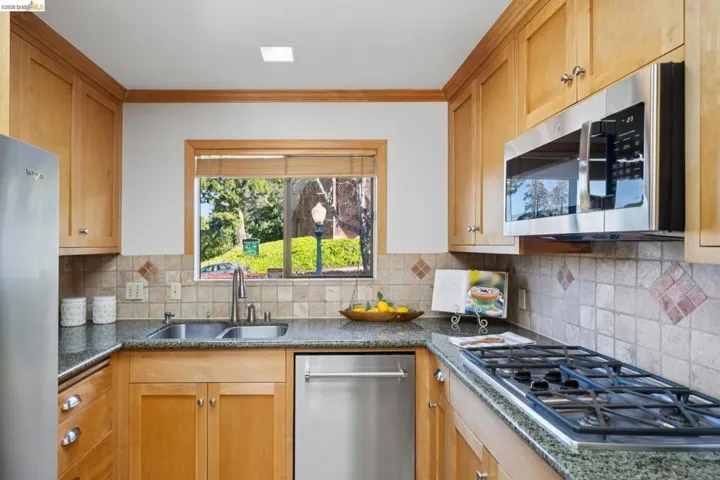 Kitchen with stainless steel appliances, dark stone counters, ornamental molding, and tasteful backsplash