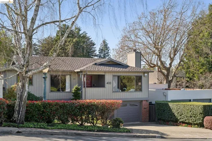 View of front of property featuring a chimney, driveway, a garage, brick siding, and covered porch