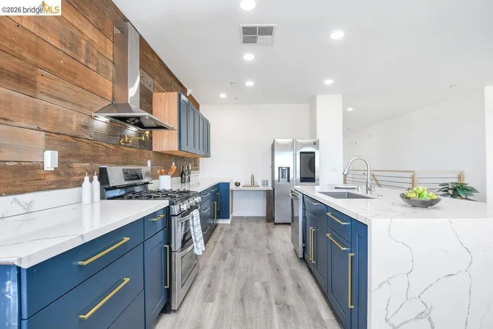 Kitchen featuring stainless steel appliances, light stone counters, ventilation hood, blue cabinetry, and recessed lighting