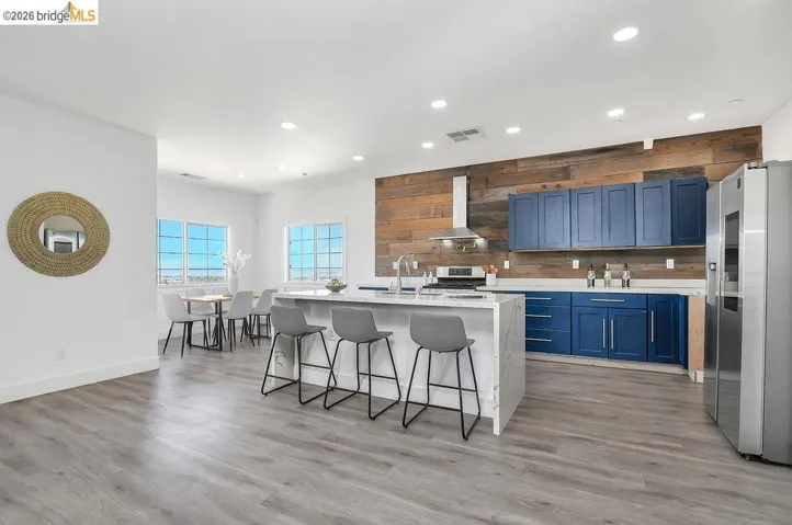 Kitchen with recessed lighting, stainless steel appliances, a kitchen breakfast bar, an island with sink, and light stone counters