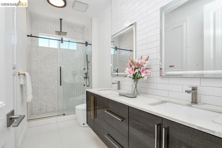 Full bath featuring double vanity, a stall shower, decorative backsplash, and light tile patterned floors